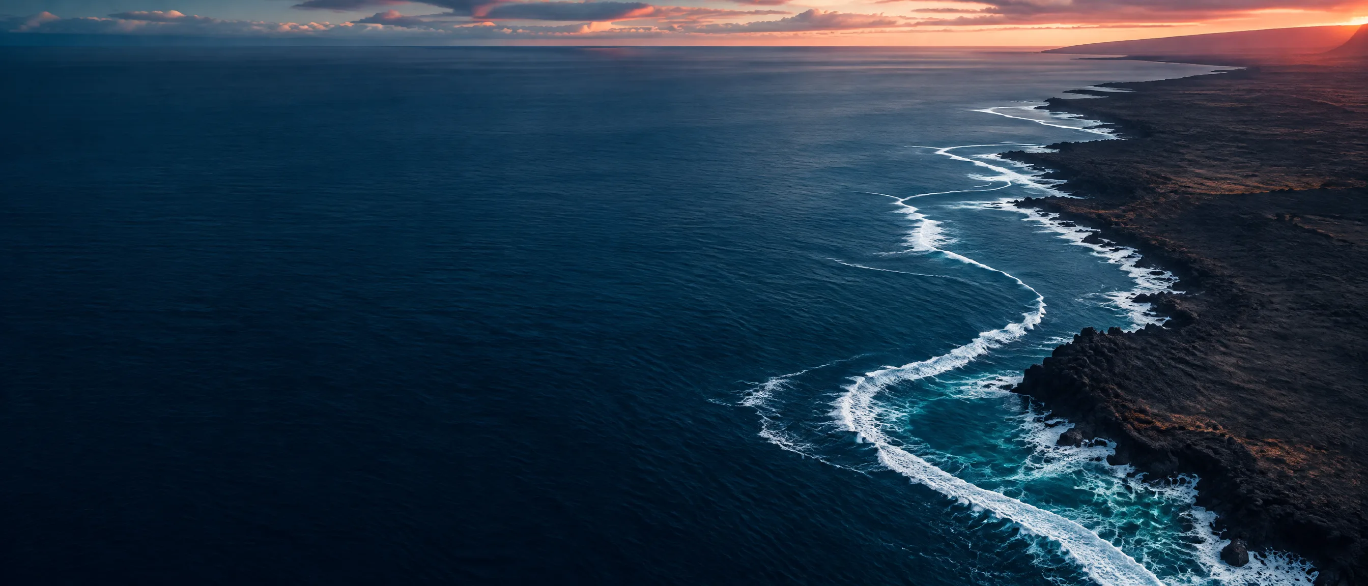Aerial view of Pacific surf meeting a volcanic Hawaiʻi coastline at dusk
